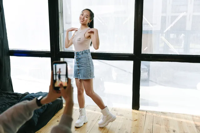 A young woman dancing while being recorded on a smartphone in a sunlit modern studio. Short form video marketing: refresh your skills forecast